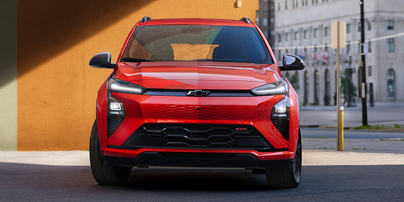 Red 2027 Chevrolet Bolt EV front view parked outdoors, showcasing the modern grille design, LED headlights, and compact electric hatchback styling.
