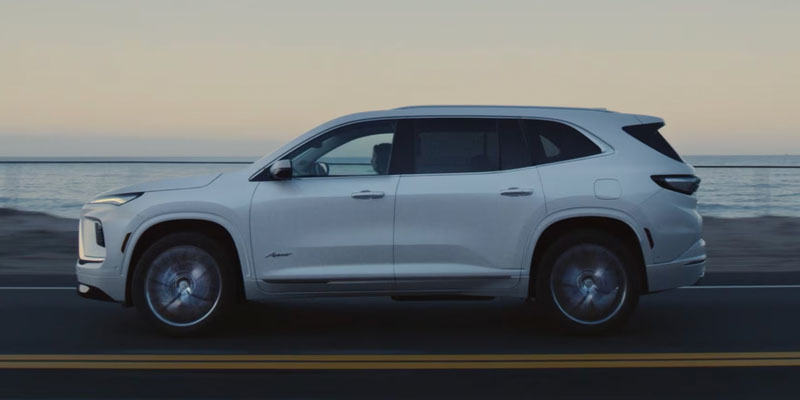 A white Buick Enclave driving along a coastal road at sunset.